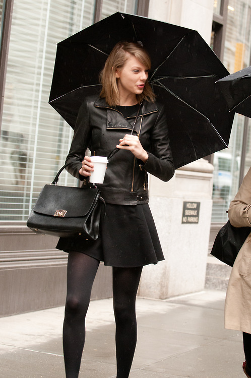 Taylor Swift in Black Leather Jacket with drink and umbrella on hand.